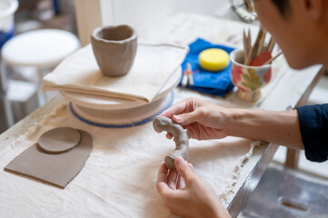 Close up of pottery artist's hand molding clay into a mug handle at working table in class or studio