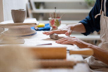 Close up of pottery artist's hand molding a clay mug's handle at working table in a class or studio.