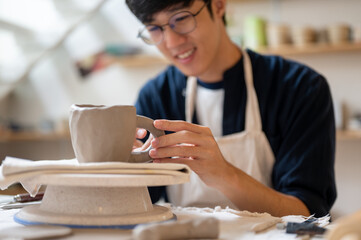 Pottery artist holding handle add to clay mug on throwing wheel at working table in a class or...