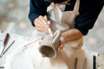 Young pottery artist using a modeling tool to smooth a clay mug at working table in class or studio