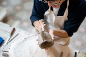 Young pottery artist holding modeling tool pressing on clay mug at working table in class or studio