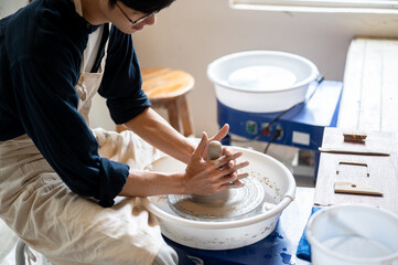 Young pottery artist's with stained hands molding a clay on spin throwing wheel in a class or studio
