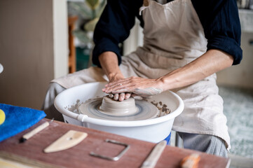 Close up of pottery artist's stained hands pressing a clay on throwing wheel in a class or studio.