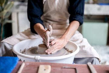 Close up of pottery artist's stained hands smoothing a clay on throwing wheel in a class or studio.