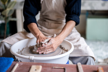 Close up of pottery artist's stained hands molding up a clay on throwing wheel in a class or studio.