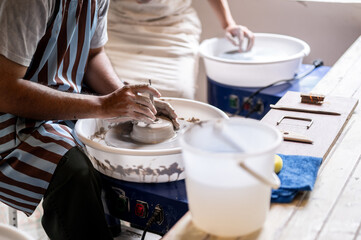 Close up of pottery artist using tool to a make hole on clay on throwing wheel in class or studio.