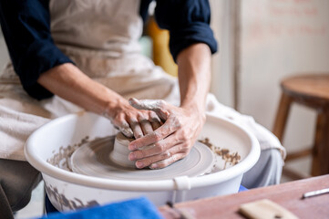 Close up of pottery artist's stained hands covering a clay on throwing wheel in a class or studio.