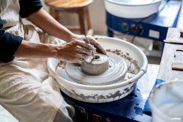 Close up of pottery artist using tool opening a hole on clay on throwing wheel in class or studio.