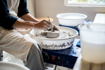 Close up of pottery artist using tool making a hole on clay on throwing wheel in class or studio.