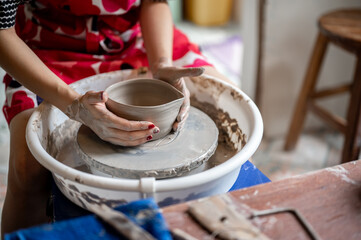 Painted nail woman pottery artist holding clay tea brewing bowl on throwing wheel in class or studio