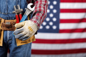 Worker wearing gloves holding tools with blurred United States flag background, labor day and industrial work concept