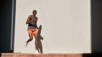 Athletic man jogging outdoors in sunny weather against a wall
