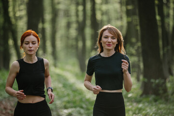 Two women jogging in a lush forest trail