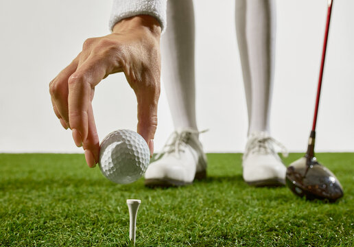 Hand placing golf ball on tee with player shoes in background. Concept of women clubs education, wellness coaching, and branding for female-focused golf instruction content.