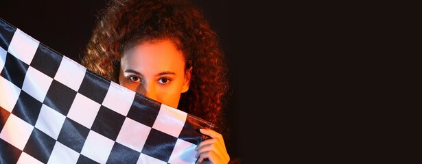 Beautiful young woman holding racing flag on dark background with space for text