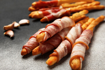 Tasty Italian Grissini with bacon on grunge background, closeup