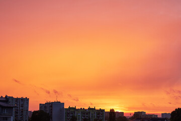 Obraz premium Vibrant orange and pink sky at sunset over urban apartment buildings and city silhouette, showcasing beautiful atmospheric colors and an atmospheric golden hour glow