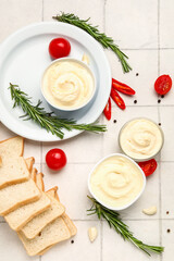Bowls of tasty cream cheese and fresh bread on white tile background