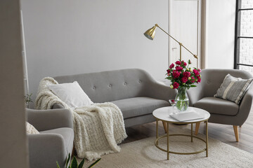Vase with red peonies, glass and laptop on coffee table in living room
