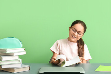 Little girl doing lessons at table on green background