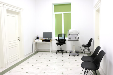 A modern ophthalmology office with an autorefractor, black patient chairs, a white marble floor...