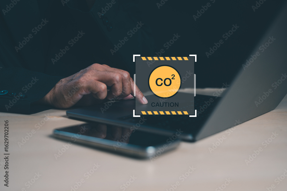 Poster a person types on a laptop while a caution symbol related to co2 emissions is displayed, highlightin