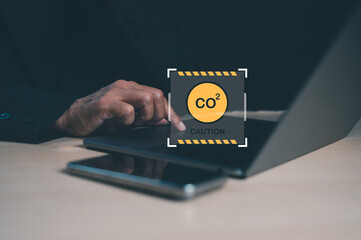 A person types on a laptop while a caution symbol related to CO2 emissions is displayed, highlighting environmental awareness and technology use.