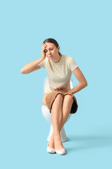 Young woman suffering from cystitis on toilet bowl against blue background