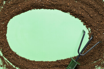 Frame made of soil with gardening rake on green background