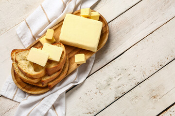 Board with fresh butter and bread on white wooden background