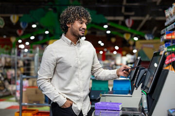 A man pays with his phone at a self-checkout machine in a grocery store. The scene conveys modern shopping.