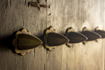 View of aged wooden door adorned with ornate brass knobs, their conical shapes catching the light in a warm glow, Lamu, Kenya.