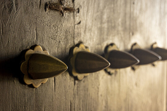 View of aged wooden door adorned with ornate brass knobs, their conical shapes catching the light in a warm glow, Lamu, Kenya.
