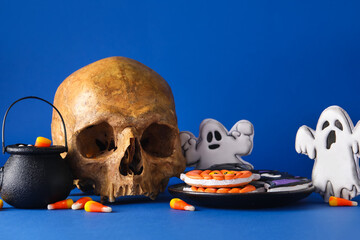 Plate with tasty cookies, candy corns and skull for Halloween celebration on blue background