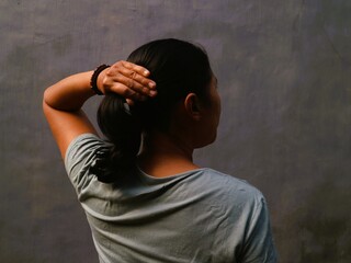 Asian Indonesian woman, seen from behind, is putting her hair up with a focused and casual gesture.