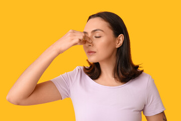 Young woman touching her nose on yellow background