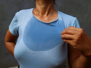Asian Indonesian woman with stain on t-shirt sweat patch on chest and neck against gray background....