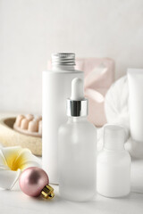 Bottles of cosmetic products and Christmas ball on light background