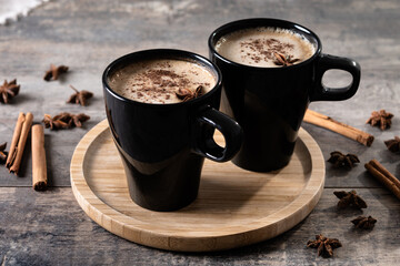 Chai Latte in Black Mug with Spices( star anise and cinnamon) on wooden table. 