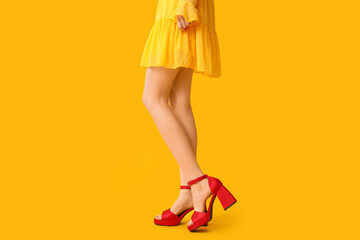 Legs of beautiful young woman in stylish high heels on yellow background