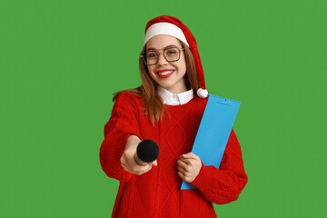 Young female journalist in Santa hat on green background