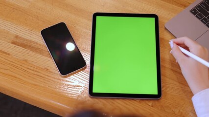 Person is writing on a green tablet with a white pen. A cell phone is on the table next to the tablet