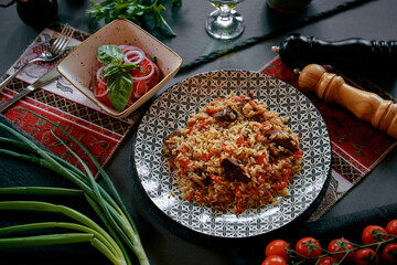 A vibrant plate of aromatic rice dish featuring tender meat, surrounded by fresh herbs, vegetables,...