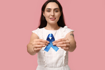 Pretty young woman with blue ribbon on pink background. Colon cancer awareness concept