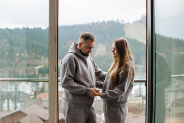 Expecting couple holding hands and embracing on balcony with mountain view