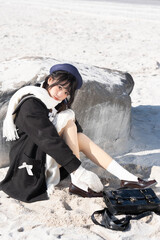 Young Asian woman relaxed on sandy beach with stylish outfit.