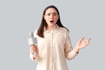 Shocked female reporter in earphone with microphone on light background