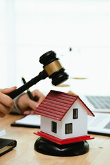 A person types on a laptop near a house model, gavel, and contract, representing real estate law,...