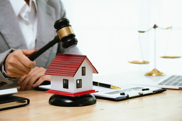 A person types on a laptop near a house model, gavel, and contract, representing real estate law,...