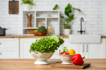 Colander with fresh vegetables on wooden kitchen counter